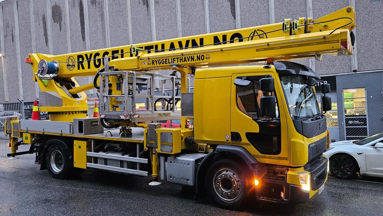 Gul liftbil fra Rygge Lift og Havn parkert foran industribygg med løftearmen senket.